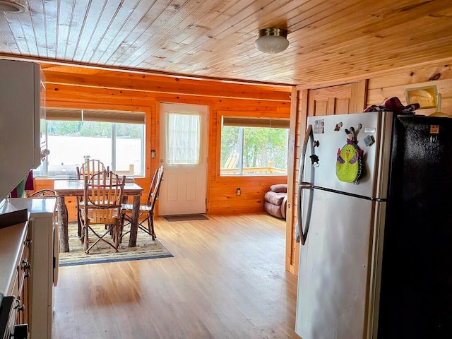 kitchen with wood walls, plenty of natural light, stainless steel fridge, and light wood-type flooring