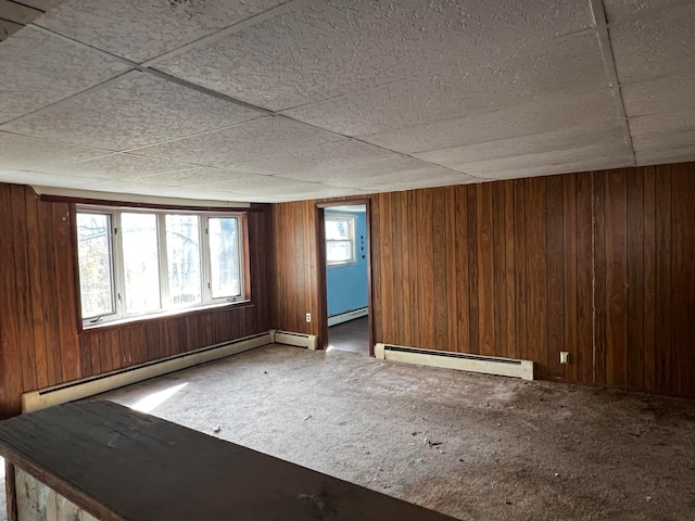 carpeted spare room featuring a healthy amount of sunlight, wooden walls, and a baseboard heating unit