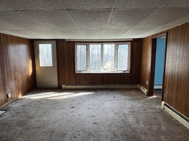 carpeted spare room featuring a paneled ceiling, wooden walls, and a baseboard heating unit