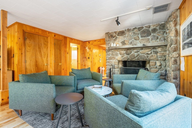 living room featuring wood walls, a stone fireplace, and wood-type flooring