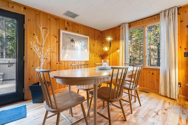 dining area featuring wooden walls, light hardwood / wood-style floors, and a healthy amount of sunlight