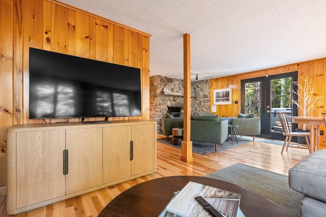 living room featuring a stone fireplace, wooden walls, light hardwood / wood-style flooring, and french doors