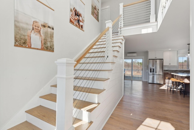 staircase featuring hardwood / wood-style floors, a high ceiling, and a wall unit AC