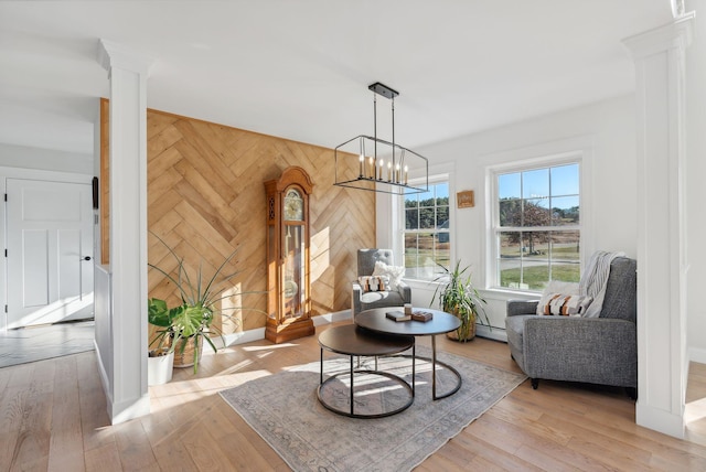 sitting room featuring an inviting chandelier, baseboard heating, light hardwood / wood-style flooring, decorative columns, and wood walls