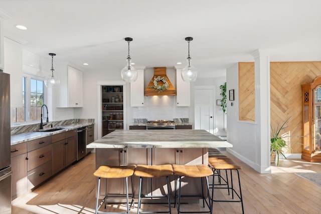 kitchen featuring white cabinetry, sink, light wood-type flooring, custom exhaust hood, and appliances with stainless steel finishes