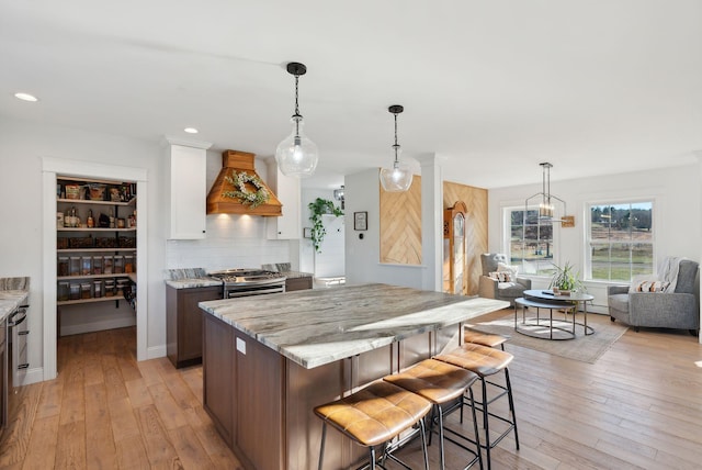 kitchen featuring gas stove, custom range hood, white cabinetry, and light hardwood / wood-style flooring