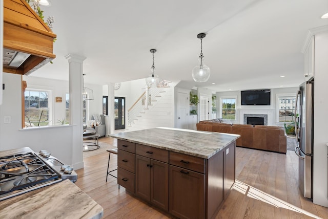 kitchen featuring pendant lighting, light hardwood / wood-style flooring, appliances with stainless steel finishes, a kitchen island, and light stone counters