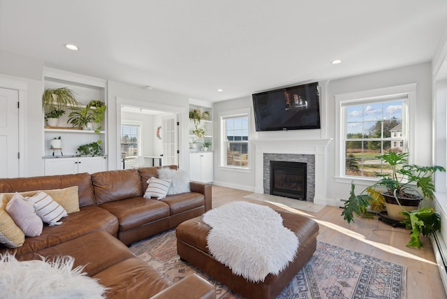 living room with light wood-type flooring, a baseboard radiator, a stone fireplace, and a healthy amount of sunlight