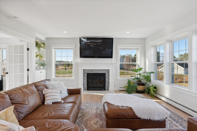 living room with a fireplace, light wood-type flooring, baseboard heating, and a wealth of natural light