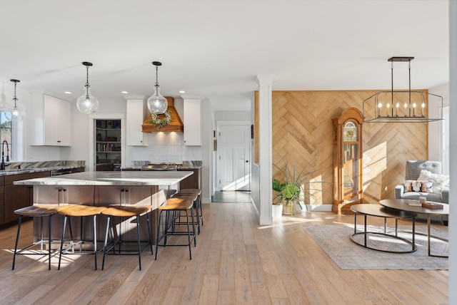 kitchen featuring white cabinets, a spacious island, hanging light fixtures, and wooden walls