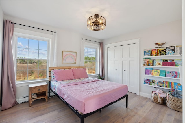 bedroom featuring a closet, wood-type flooring, a baseboard radiator, and multiple windows