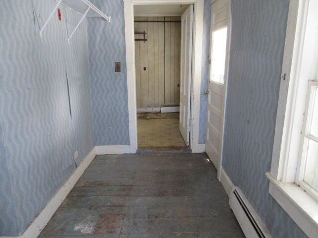 hall with dark wood-type flooring, wooden walls, and a baseboard heating unit