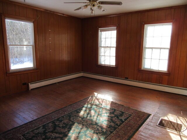 spare room with hardwood / wood-style flooring, ceiling fan, a healthy amount of sunlight, and wood walls