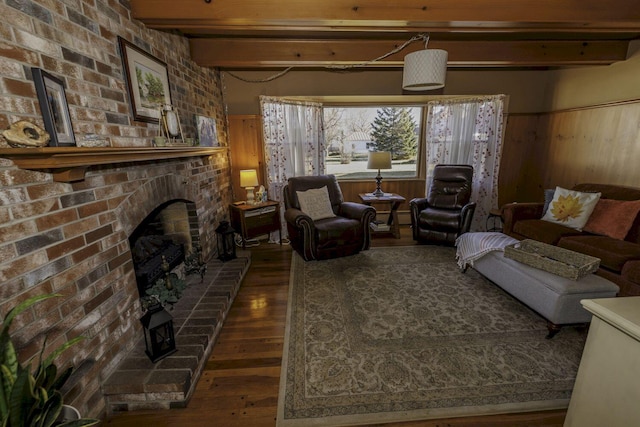 living room with beam ceiling, wooden walls, dark wood-type flooring, and a brick fireplace