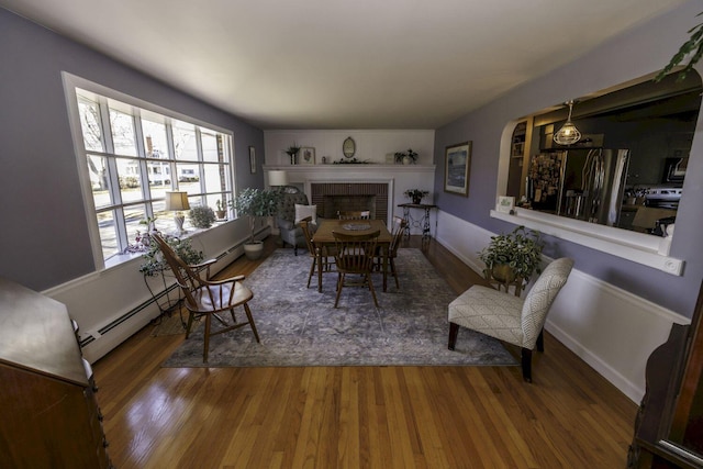 dining area with hardwood / wood-style floors, a baseboard heating unit, and a brick fireplace