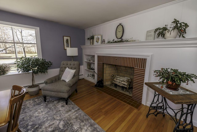 sitting room featuring wood-type flooring, a baseboard radiator, and a brick fireplace