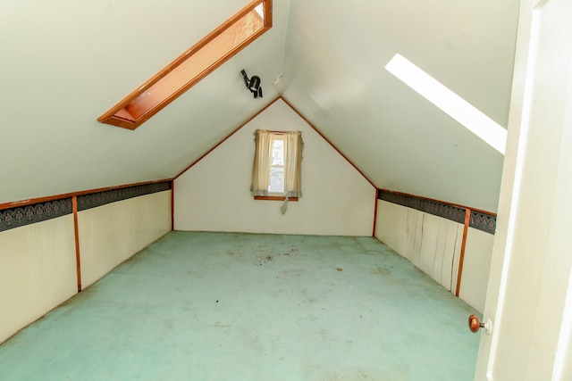 additional living space featuring vaulted ceiling with skylight and light carpet