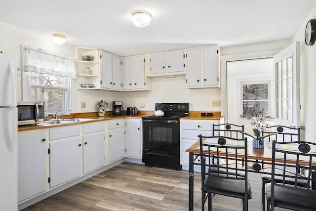 kitchen featuring black range with electric stovetop, sink, white refrigerator, light hardwood / wood-style floors, and white cabinets