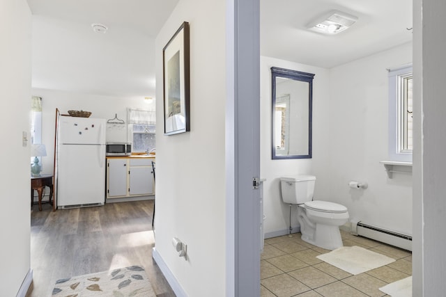 corridor with light wood-type flooring, sink, and a baseboard heating unit