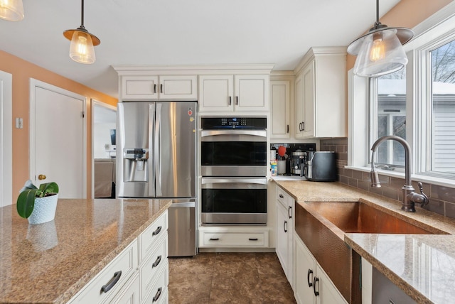 kitchen with appliances with stainless steel finishes, tasteful backsplash, hanging light fixtures, light stone counters, and sink