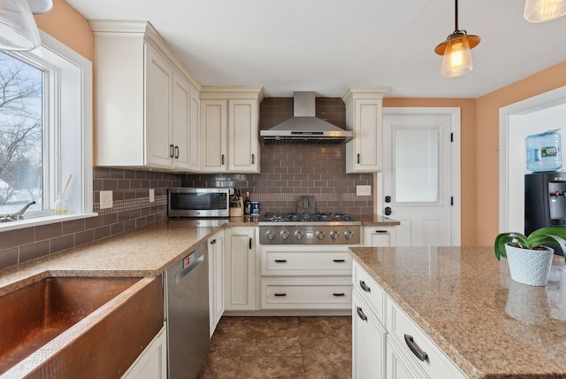 kitchen featuring stainless steel appliances, hanging light fixtures, wall chimney range hood, and backsplash