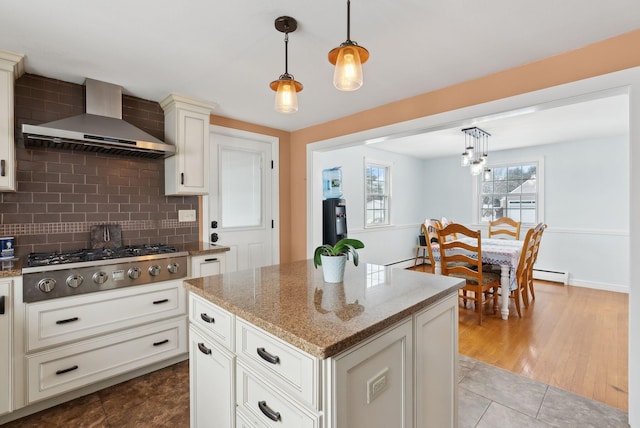 kitchen featuring a center island, pendant lighting, light stone countertops, wall chimney exhaust hood, and stainless steel gas cooktop