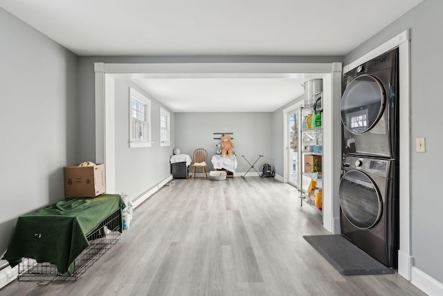 laundry room featuring light hardwood / wood-style floors, stacked washer / drying machine, and a baseboard heating unit