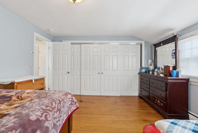 bedroom with light hardwood / wood-style floors, lofted ceiling, and a closet