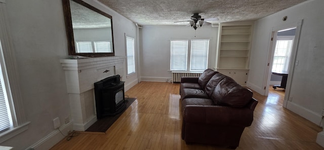 28 Maine Ave, Millinocket, ME 04462 - living room featuring radiator heating unit, a ceiling fan, a textured ceiling, a wood stove, and plenty of natural light