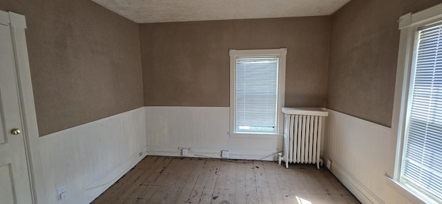 28 Maine Ave, Millinocket, ME 04462 - empty room with radiator heating unit, hardwood / wood-style flooring, and a wainscoted wall