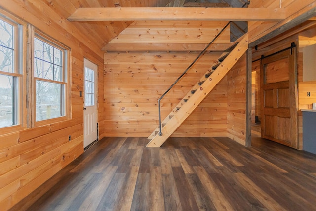 empty room with dark hardwood / wood-style flooring, lofted ceiling with beams, a barn door, and wooden walls