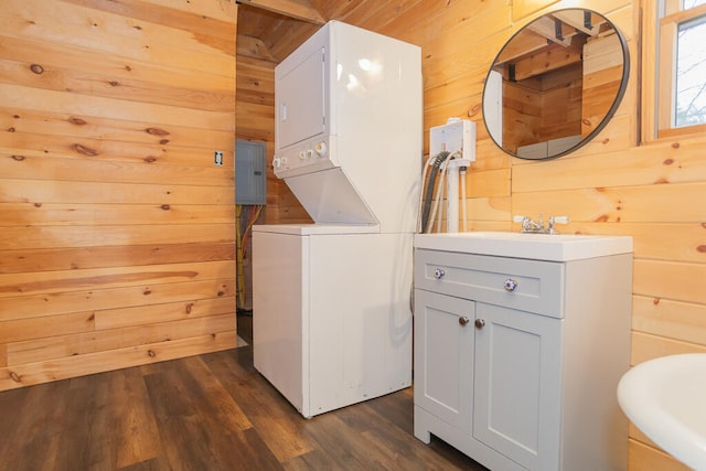 clothes washing area with stacked washer / dryer, wooden walls, sink, and dark hardwood / wood-style floors