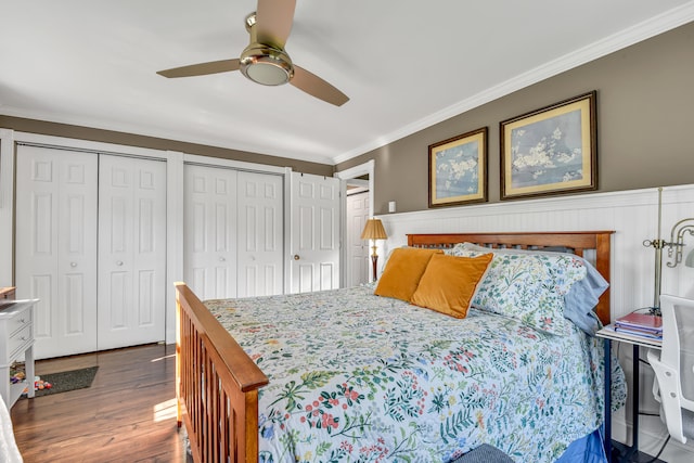 bedroom featuring dark wood-type flooring, two closets, ceiling fan, and crown molding