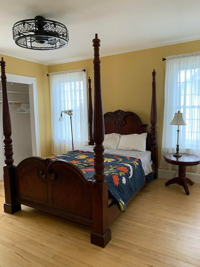 bedroom featuring light wood-type flooring, a closet, multiple windows, and crown molding