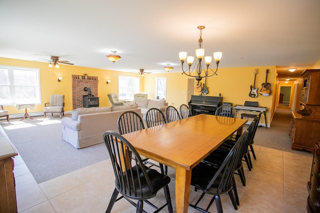 dining room featuring ceiling fan with notable chandelier, a wood stove, and light tile patterned flooring