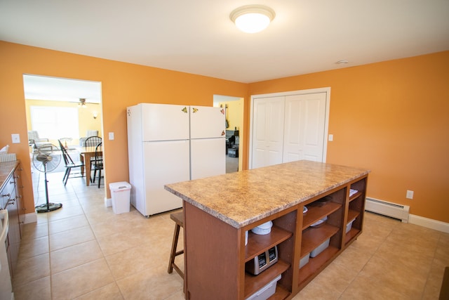 kitchen featuring ceiling fan, a center island, a baseboard heating unit, white refrigerator, and light tile patterned floors