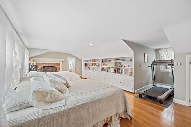 bedroom with light hardwood / wood-style flooring, lofted ceiling, and a brick fireplace