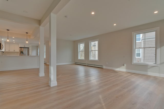 unfurnished living room featuring a healthy amount of sunlight, sink, a baseboard radiator, and light wood-type flooring