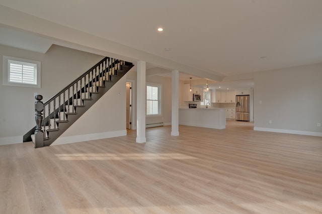 unfurnished living room featuring a baseboard heating unit, light hardwood / wood-style flooring, a healthy amount of sunlight, and sink