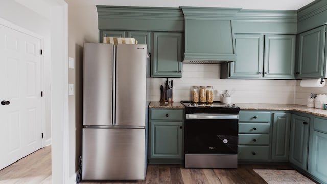 kitchen with premium range hood, wood-type flooring, stone countertops, decorative backsplash, and appliances with stainless steel finishes