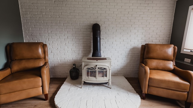 sitting room featuring hardwood / wood-style floors, a wood stove, and brick wall