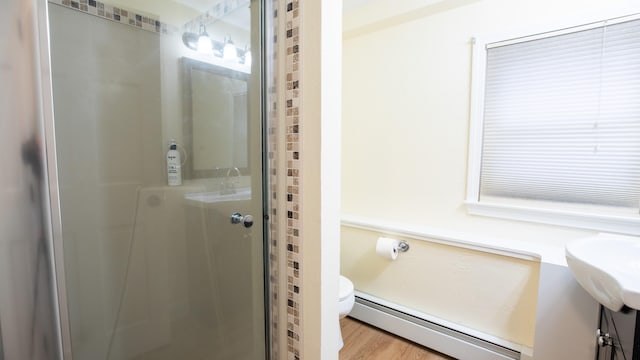 bathroom with a shower with shower door, toilet, wood-type flooring, and baseboard heating