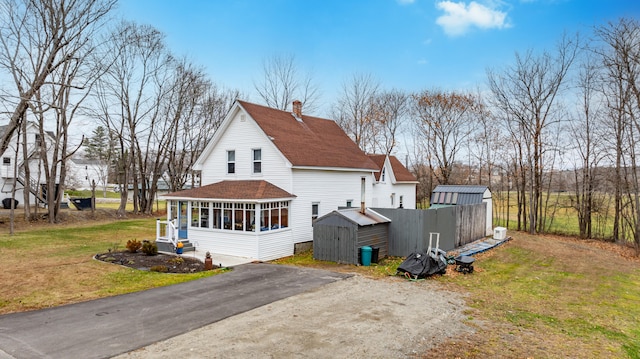 back of property featuring a lawn, a sunroom, and a storage unit