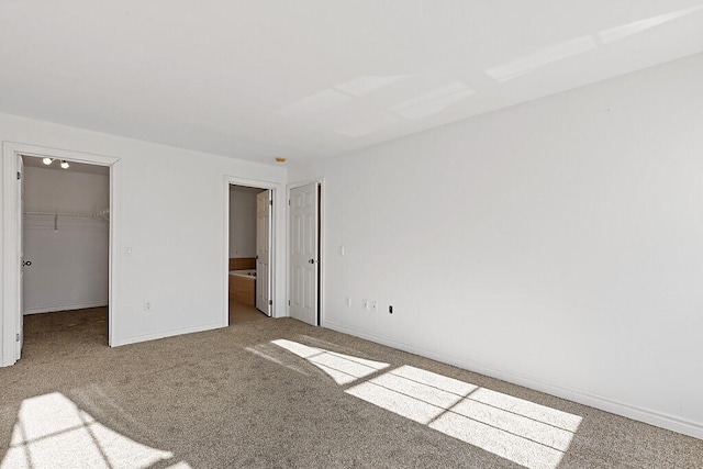 unfurnished bedroom with a walk in closet, a closet, ensuite bath, and light colored carpet