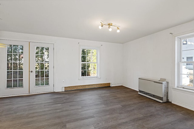 empty room featuring heating unit, a healthy amount of sunlight, dark wood-type flooring, and a baseboard radiator