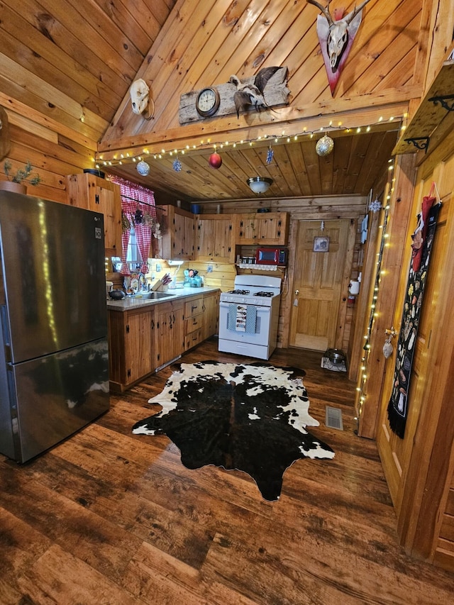 kitchen with white gas range, sink, dark hardwood / wood-style flooring, refrigerator, and wooden walls