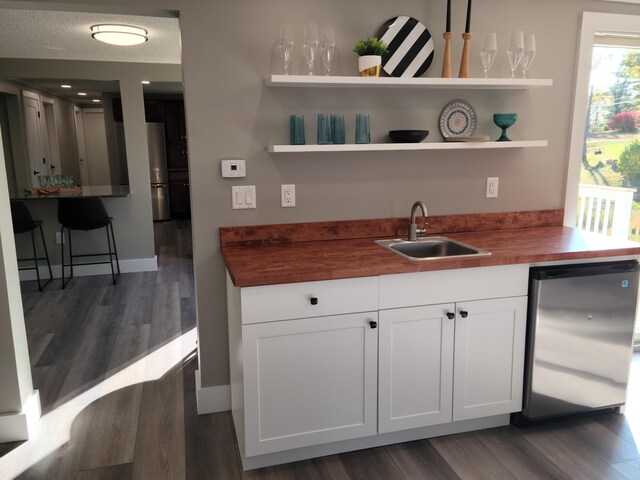 kitchen with a textured ceiling, sink, white cabinets, dark hardwood / wood-style floors, and butcher block counters