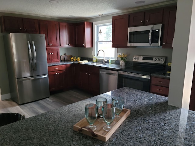 kitchen with appliances with stainless steel finishes, a textured ceiling, sink, light hardwood / wood-style flooring, and dark stone countertops