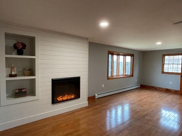 2 Old County Rd, Veazie, ME 04401 - unfurnished living room featuring a baseboard radiator, baseboards, wood finished floors, a fireplace, and built in shelves