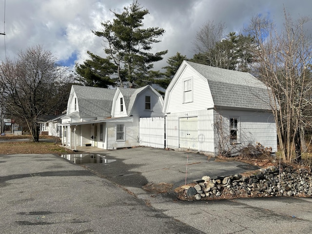 view of front of home with driveway, a garage, a shingled roof, a gambrel roof, and an outbuilding